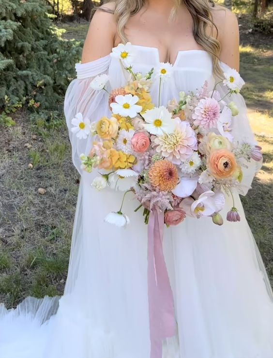 a subtle wedding bouquet of pink and yellow dahlias, ranunculus, poppies and long pink ribbons for a spring or summer wedding