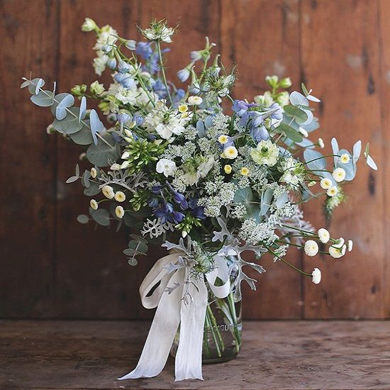 a summer wedding bouquet of neutral and blue blooms, some greenery and white ribbon with a bow is a cool solution