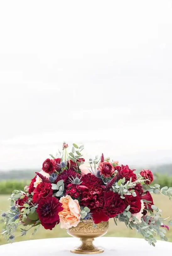 a super bold wedding centerpiece with burgundy and fuchsia blooms, peachy flowers, thistles and greenery