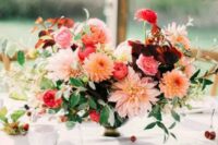 a super colorful wedding centerpiece of orange and pink dahlias, burgundy and pink ranunculus, greenery and some berries