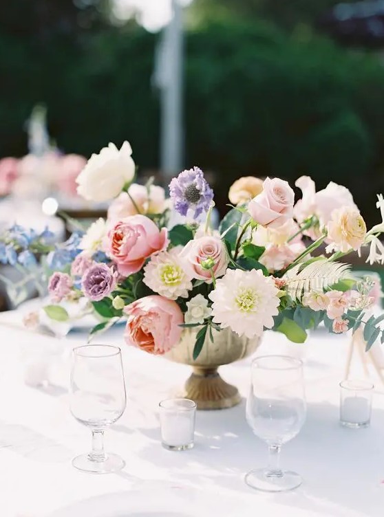 a super lush and chic pastel wedding centerpiece of pink roses and peony roses, lilac peony roses and purple ranunculus, greenery and dahlias