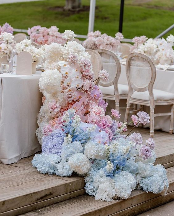 a super lush wedding table runner with white, blue and pink hydrangeas, roses, orchids that descends to the floor