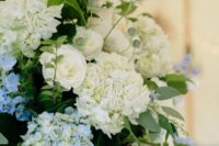 a tall and textural wedding centerpiece of blue and white hydrangeas, white roses, greenery and seed pods is a bold solution