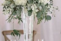 a tall wedding centerpiece of a sheer vase, white hydrangeas and various greenery and eucalyptus is chic and timeless