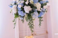a tall wedding centerpiece of blue and white hdyrangeas, white roses and greenery and candles at the base is cool and catchy