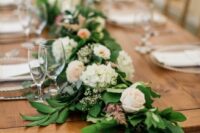 a textured wedding table runner of greenery, blush roses, white hydrangeas and some greenery is a cool idea for spring or summer