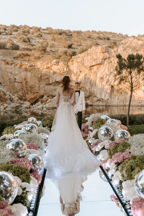 a unique wedding ceremony space with white baby's breath, greenery, pink and white hdyrangeas, disco balls and a mirror pathway plus a mountain and lake view