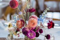 a vibrant wedding centerpiece of burgundy, purple, coral dahlias, allium, blue blooms and some berries is wow
