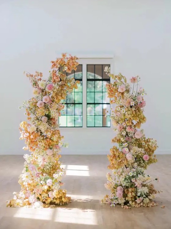 a vivacious wedding arch with light pink and blush, white and yellow blooms and some leaves is a cool idea for a bold wedding