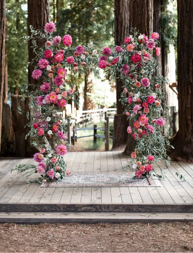 a wedding arch done with lush greenery and bold dahlias and peonies in fuchsia and pink plus deep reds