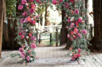 a wedding arch done with lush greenery and bold dahlias in fuchsia and pink plus deep reds