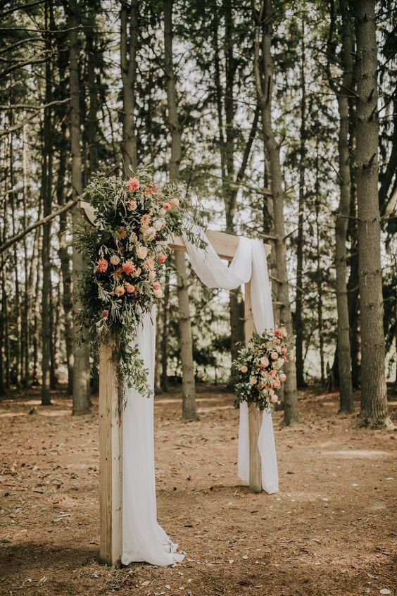 a wedding arch done with white fabric, greenery, blush and peachy blooms looks very cool and lovely and will be a nice fit for summer