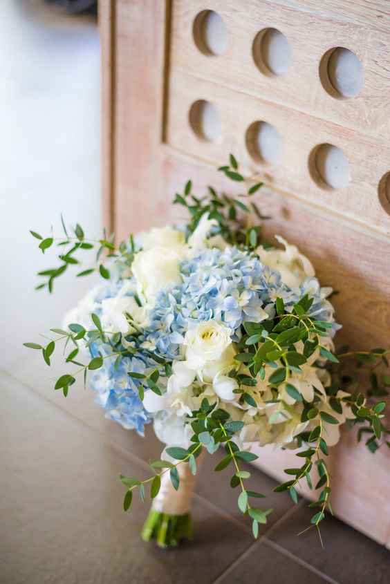 a wedding bouquet of white roses, blue hydrangeas and greenery is a light and airy arrangement that looks gorgeous