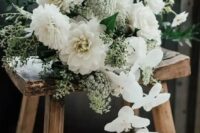 an all-white wedding bouquet of dahlias, roses, orchids, greenery and berries is a stylish idea for a modern bride
