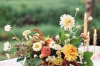 an elegant fall wedding centerpiece of red and orange dahlias, white blooms, berries, leaves and some fruit right on the table