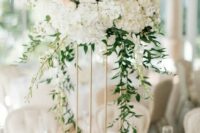 an elegant tall wedding centerpiece of white hydrangeas and roses and greenery cascading down to the table, candles