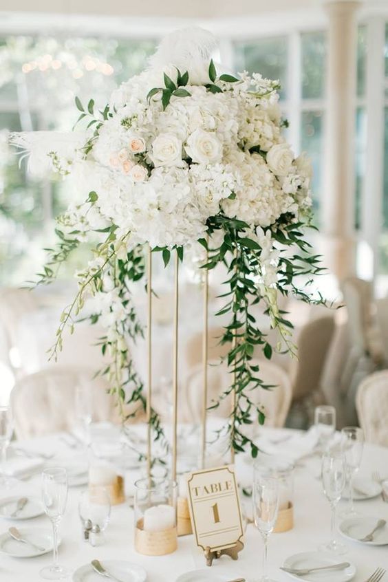 an elegant tall wedding centerpiece of white hydrangeas and roses and greenery cascading down to the table, candles