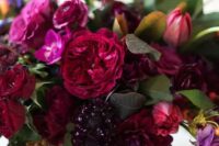 an exquisite wedding centerpiece of deep purple, burgundy, hot pink, deep red blooms and foliage is wow