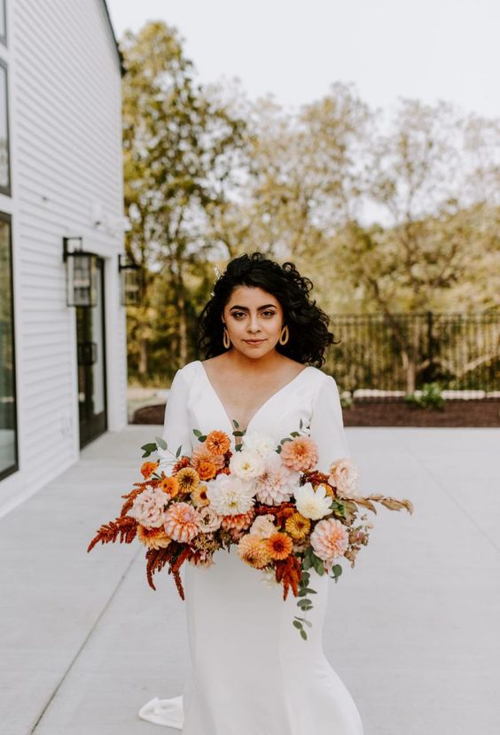 an eye-catching wedding bouquet of white, blush, yellow and peachy dahlias and greenery plus bold leaves