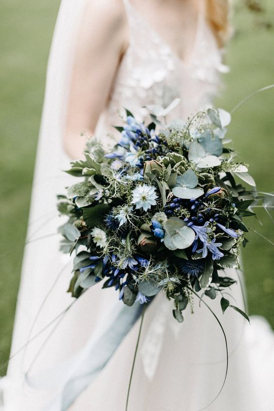 an eye-catchy wedding bouquet of white and bold blue blooms, greenery and berries, some twigs is a unique solution