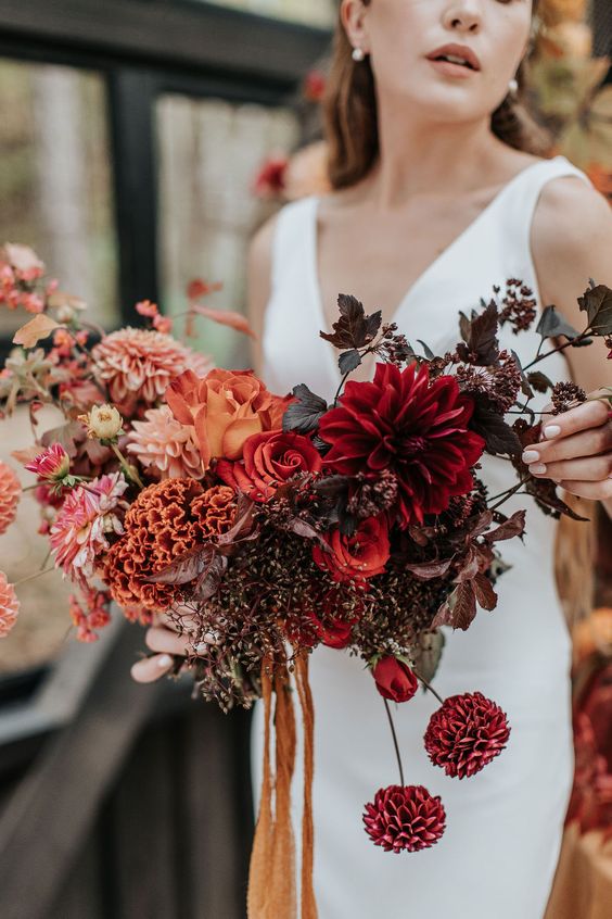 an ombre wedding bouquet of pink and burgudny dahlias, red roses, some fillers and dark foliage for a refined fall bride