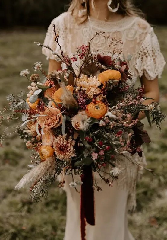 an oversized boho wedding bouquet of marigold, burgundy blooms, lots of berries, greenery and twigs