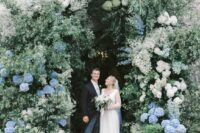 an oversized floral wedding arch done with a lot of greenery, white blooms and white and blue hydrangeas is a gorgeous idea for a spring or summer wedding