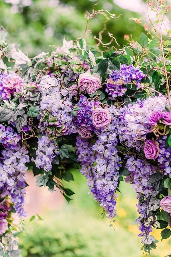 A beautiful and bold wedding arch covered with wisteria and mauve roses plus greenery and twigs for a fairy tale wedding