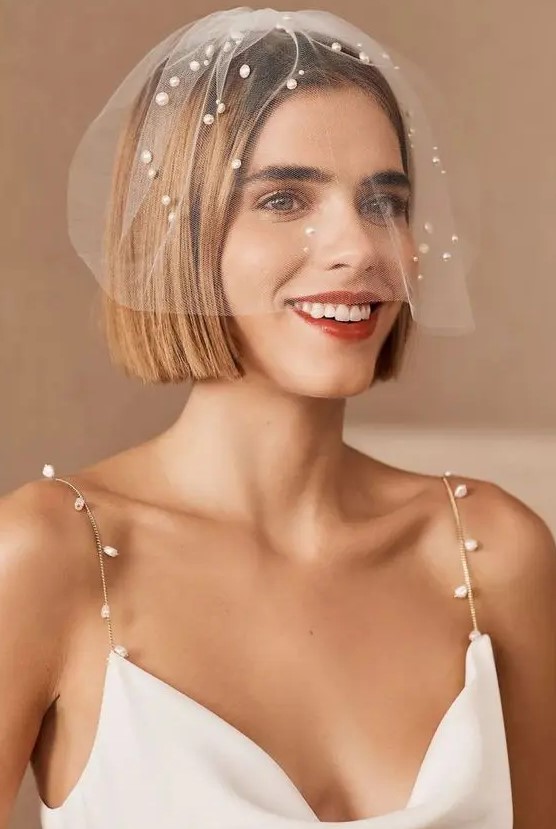 a small and elegant birdcage veil embellished with pearls randomly looks cool and matches the straps of the wedding dress