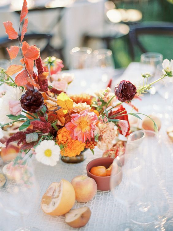 a beautiful fall wedding centerpiece of ranunculus, marigolds, roses and carnations, bold fall leaves and greenery