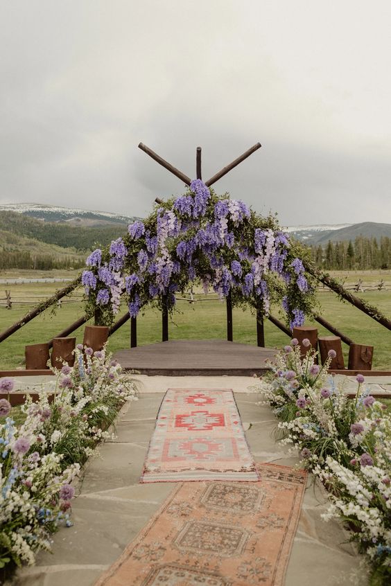 a boho wedding ceremony space with a wisteria altar, white, lilac and blue blooms and boho rugs is a cool space to enjoy