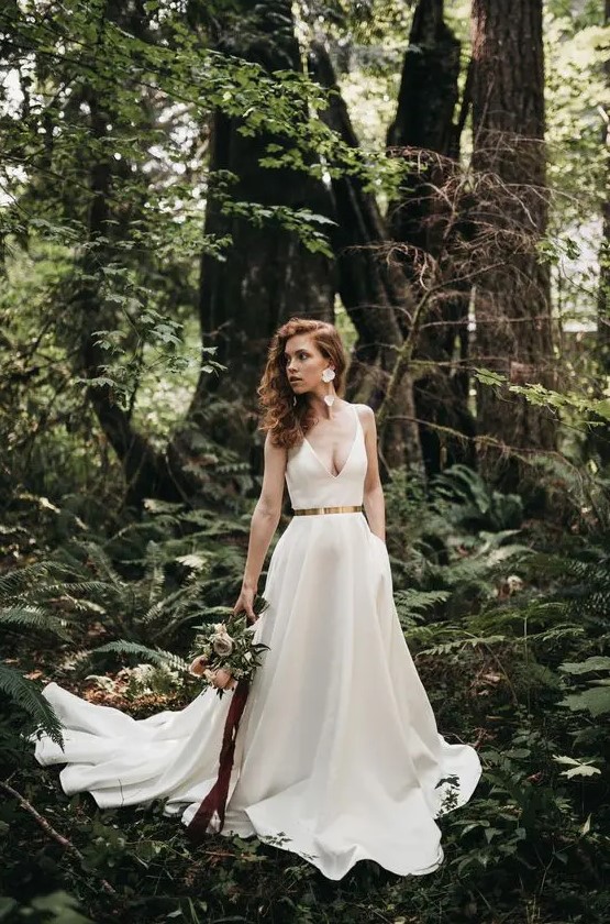 a gorgeous plain A-line wedding dress with a deep neckline, a shiny metallic belt and a pleated skirt with a long trian plus floral earrings