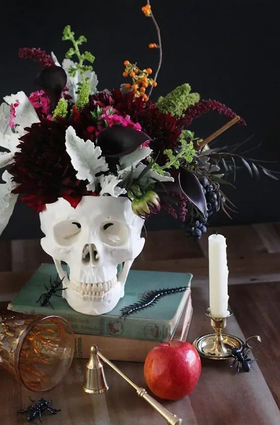 a stack of books, a skull with a dark floral arrangement with dark burgundy florals, pale and saturated greenery and berries
