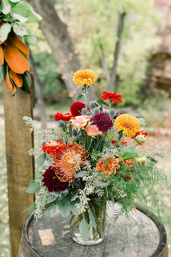 a bold wedding centerpiece of marigolds, mums and dahlias, some proteas and greenery plus thistles for a rustic wedding