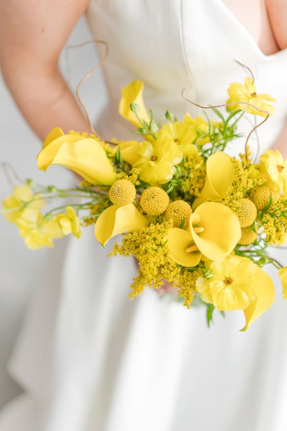a bright yellow wedding bouquet of callas, billy balls, mimosa and some twigs is a fun and bold diea for a spring or summer wedding