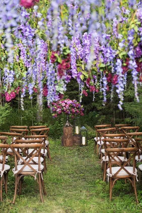 a bright wedding ceremony space with a bold and lush arrangement and wisteria and roses plus greenery hanging down is a unique blooming space