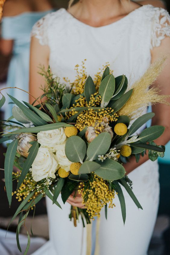 a catchy wedding bouquet of white roses, billy balls, mimosa, greenery, pampas grass is a lovely idea for a summer or fall bride