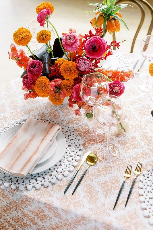 a bold wedding centerpiece of marigolds, pink ranunculus, dark leaves is a catchy solution and printed textiles paired with it look nice