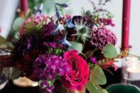 10 a bold jewel tone wedding centerpiece of purple, pink, deep purple and blue blooms, greenery and thistles and fuchsia candles around