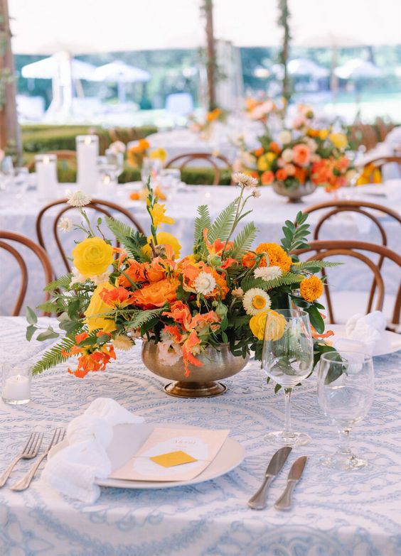 a bright tropical wedding centerpiece of yellow roses, marigolds, white chamomiles, fern and other leaves is a cool and bold idea