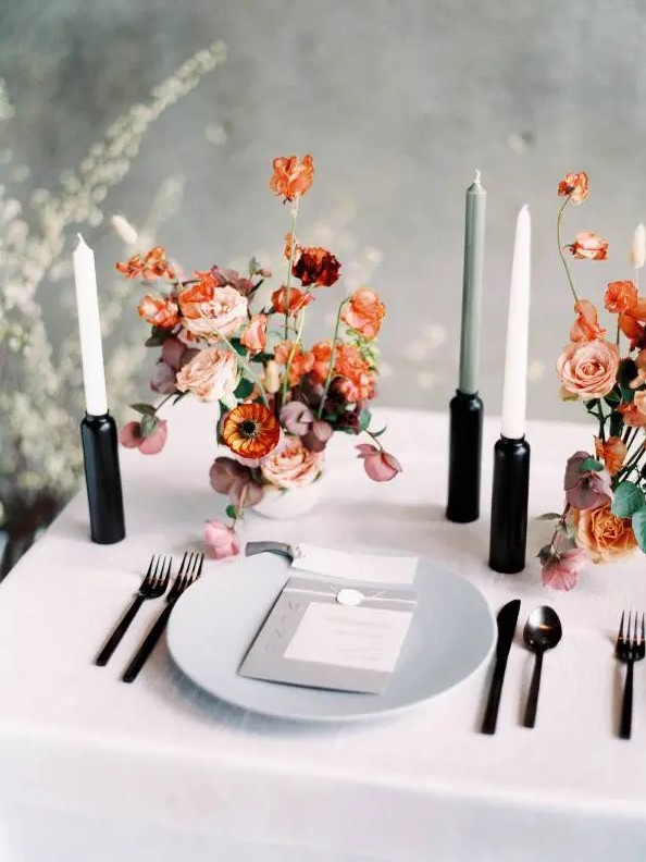 a bold minimalist wedding tablescape with neutral linens, a grey plate, black candleholders and neutral candles and bright blooms