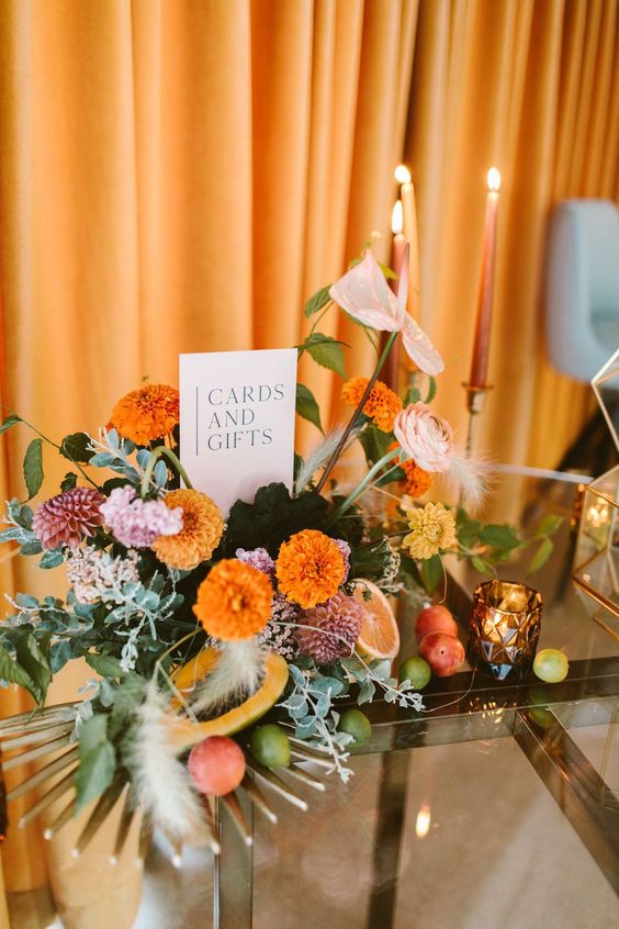 a bright wedding centerpiece of marigolds, dahlias, ranunculus and greenery plus some fronds is a cool idea for a bold wedding