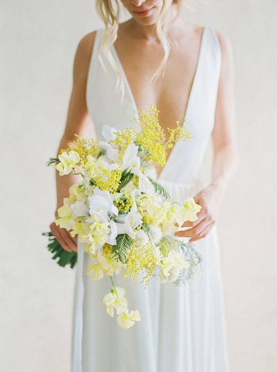 a delicate spring wedding bouquet of white and yellow blooms including mimosa and some greenery is wow
