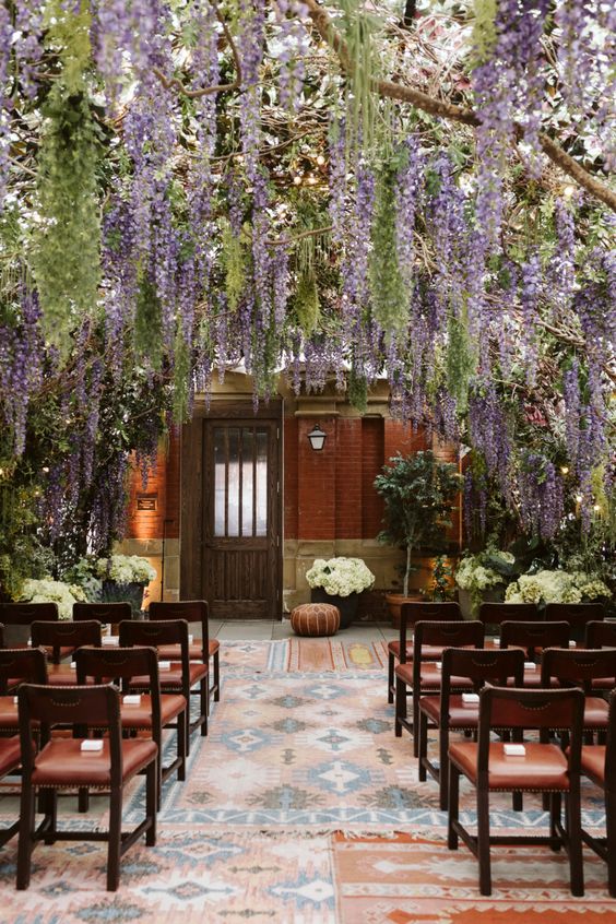 a dreamy wedding ceremony space with rows of matching chairs and wisteria naturally hanging over the space