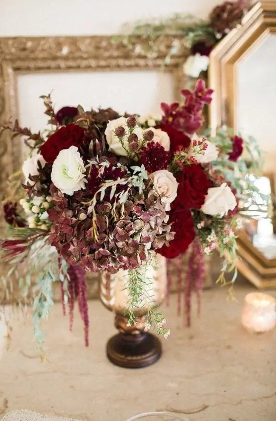 a luxurious floral centerpiece in the shades of ruby red, burgundy and white plus cascading blooms
