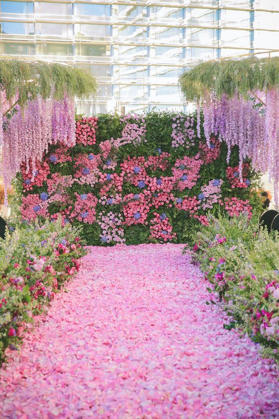 A flower filled wedding ceremony space with pink, blue, lilac blooms and greenery and petals on the floor is wow