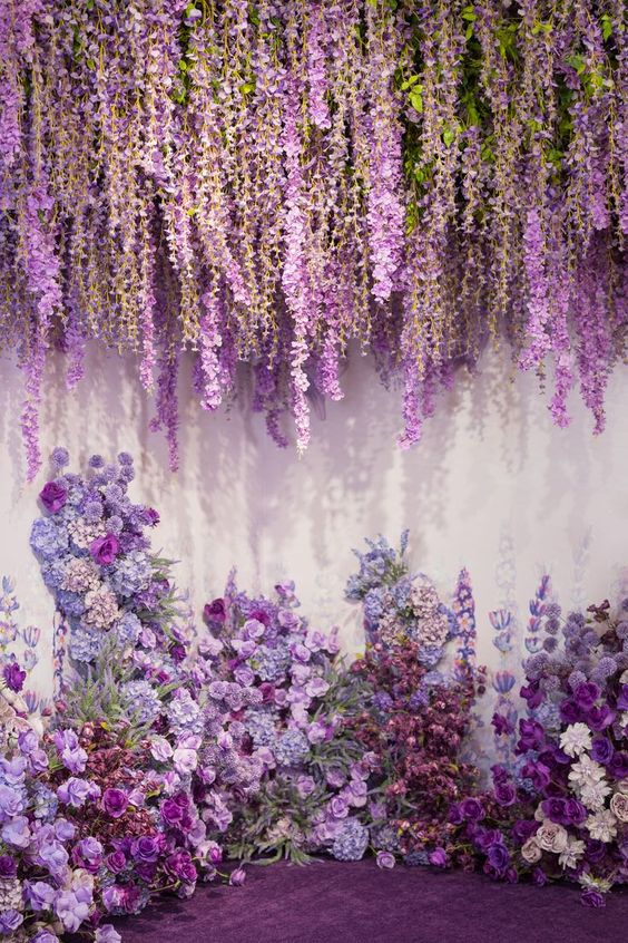 a gorgeous and lush wedding backdrop with wisteria hanging down and an altar of purple, violet and lilac blooms and greenery