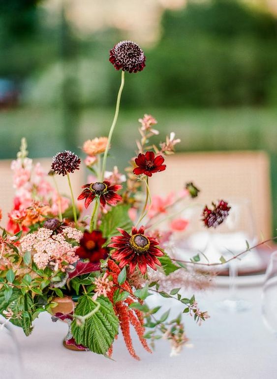 a bright fall wedding centerpiece of burgundy and deep purple blooms, pink fillers and greenery and astilbe