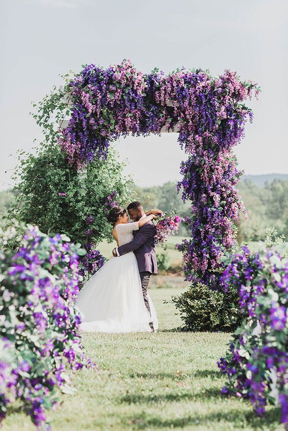 A jaw dropping wedding arch covered with greenery and wisteria and matching arrangements look jaw dropping