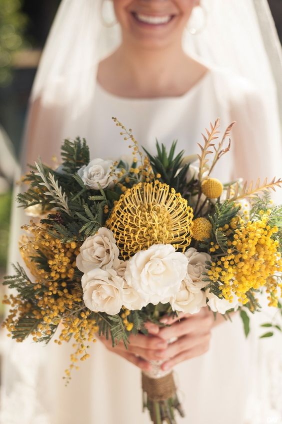 a lush wedding bouquet of white roses, a pincushion protea, mimosa, greenery and billy balls is amazing for spring or summer